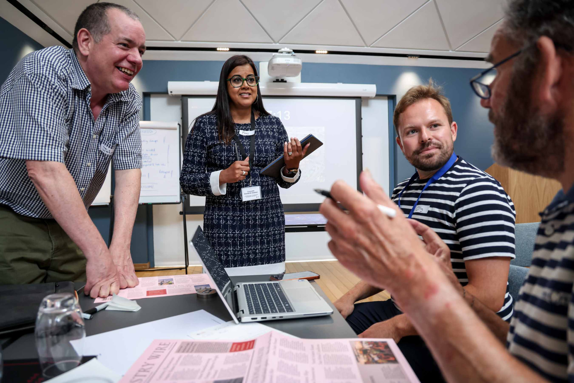 A small team in animated discussion during a 1956 session, newspaper and laptop in shot